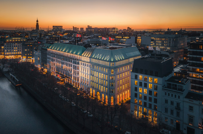 View of the Hotel Vier Jahreszeiten photographed from above at an angle across the Inner Alster, with the orange sunset visible in the background