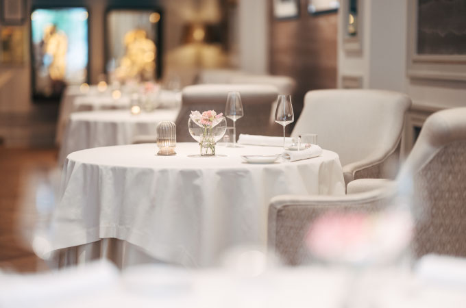 Elegantes Interieur des Restaurants Haerlin*** mit runden Tischen, die mit weißen Tischdecken gedeckt und mit Gläsern und Servietten ausgestattet sind.
