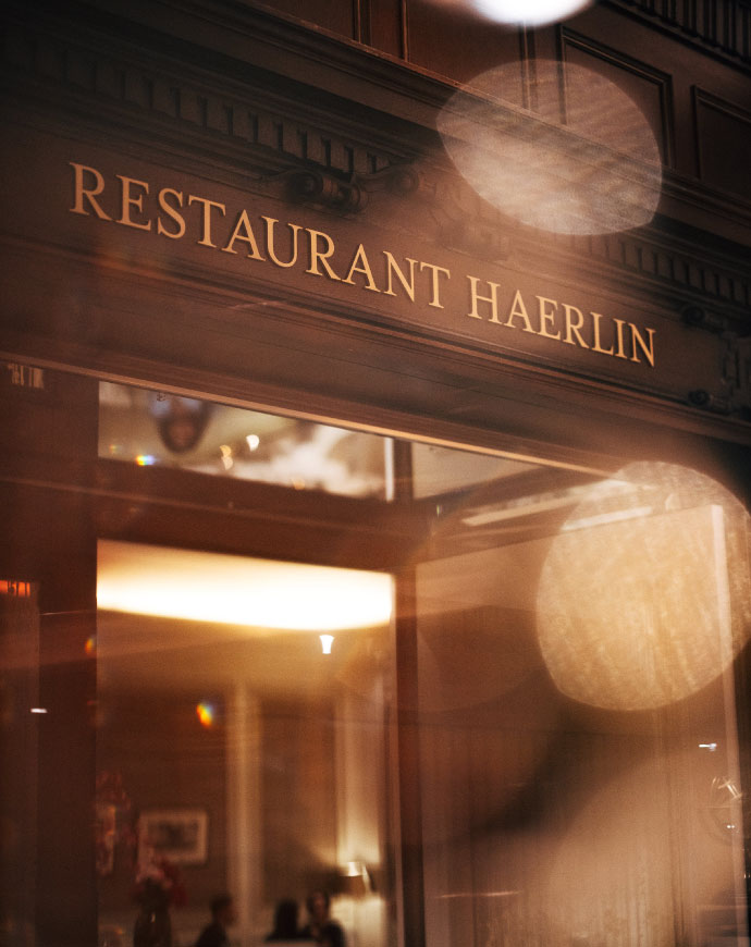 Der warm beleuchtete Eingang des Restaurant Haerlin*** mit eleganter goldener Beschriftung.