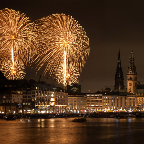 Blick über die Binnenalster auf die Gebäude und das goldene Feuerwerk am Himmel