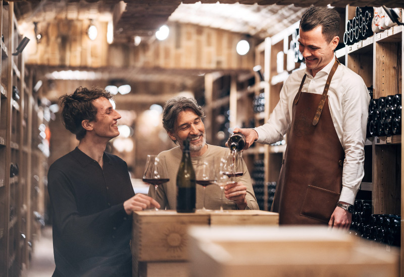 Waiter pours wine into the glasses of two guests in the wine cellar